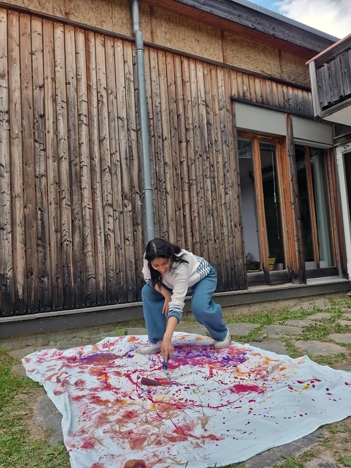 Ritty painting on a large cloth outside a wooden building