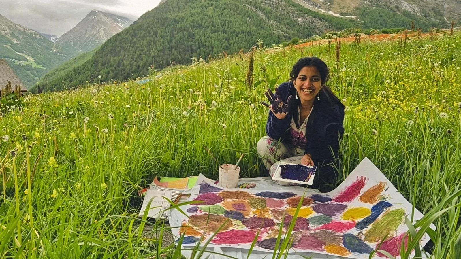 Ritty lying in an alpine meadow beside colourful paintings